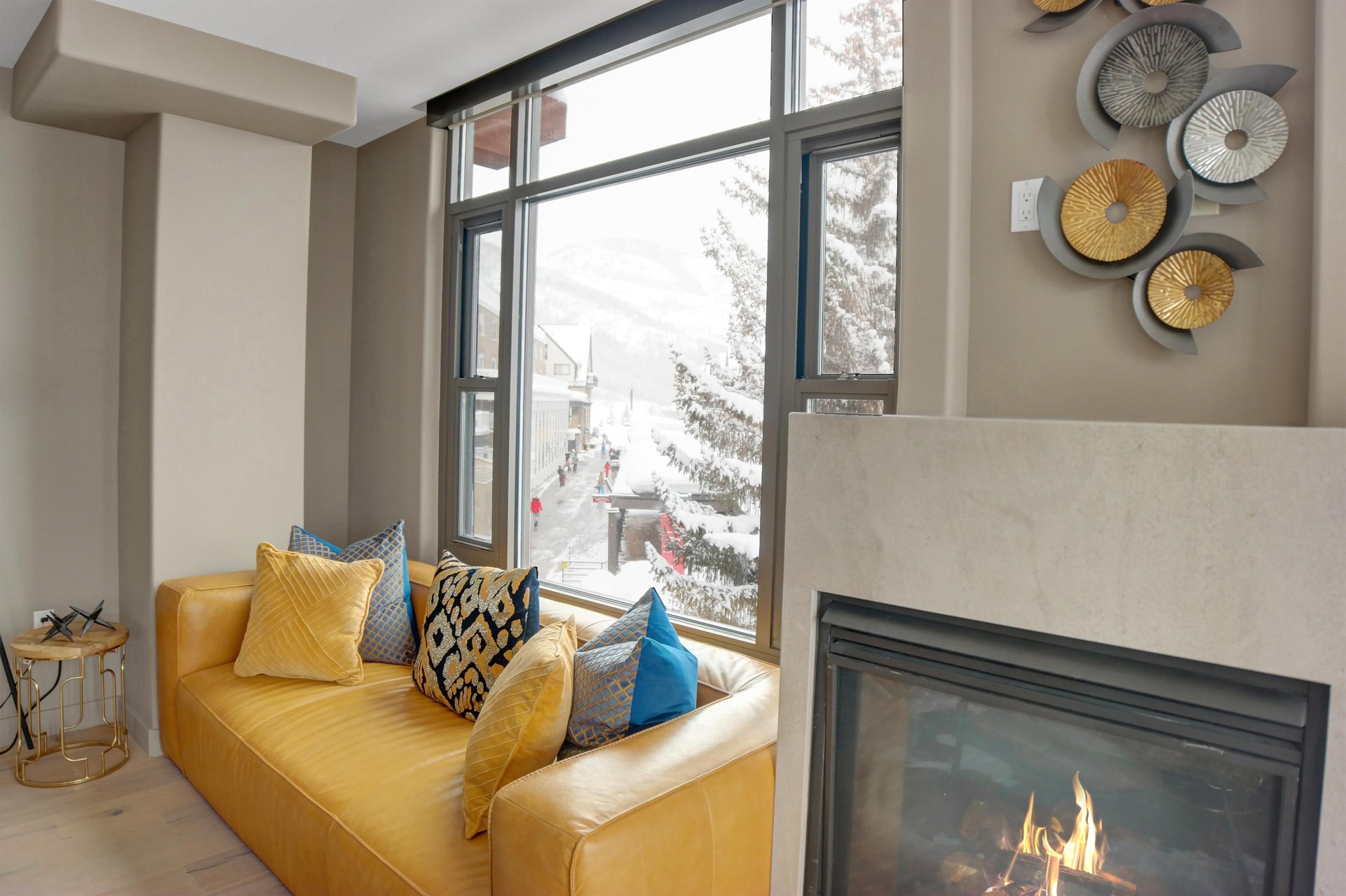 Living area with fireplace, colorful sofa and floortoceiling windows overlooking the snowy ski slopes.