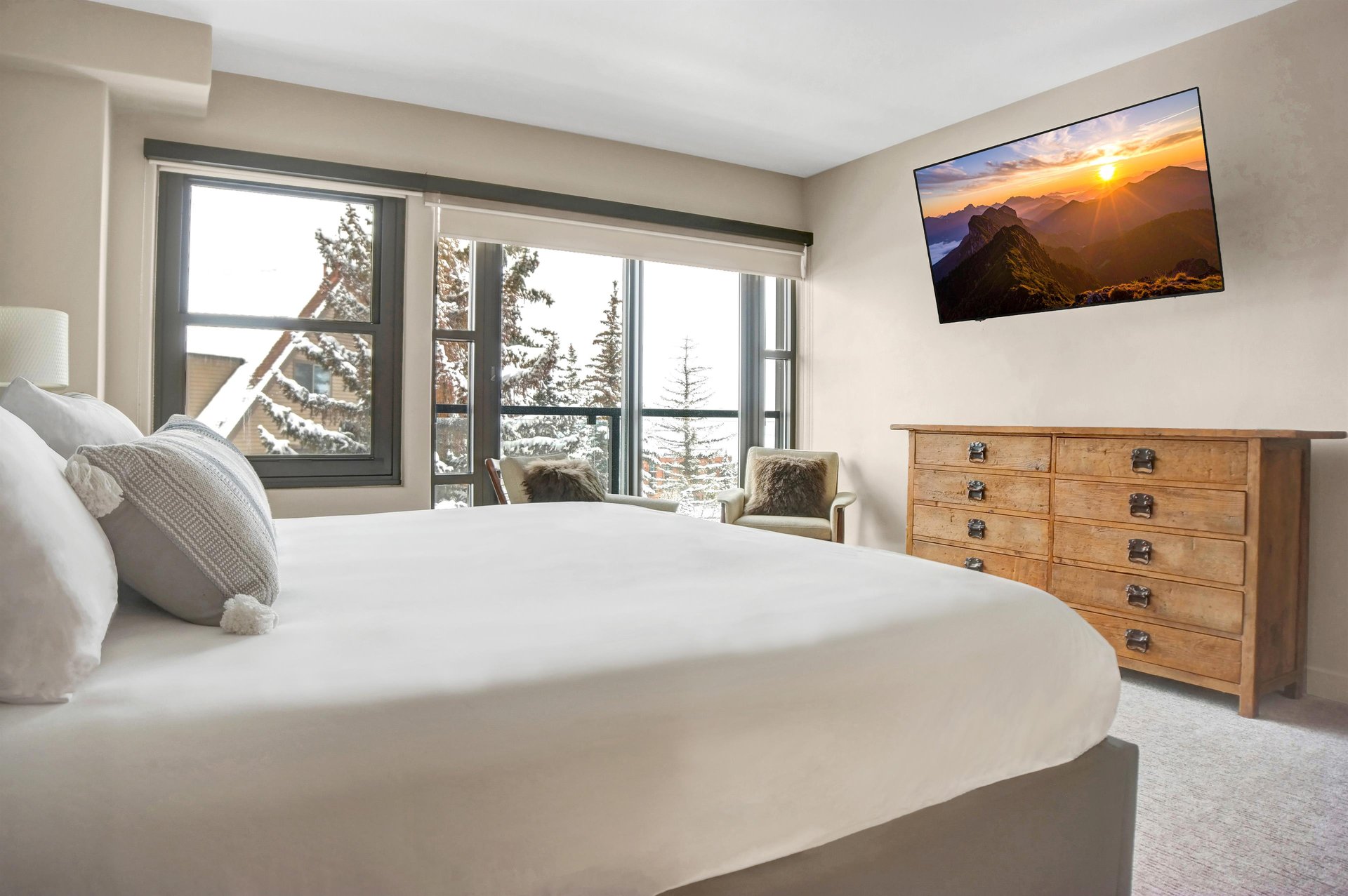 Spacious king bedroom with wood dresser, wallmounted TV and large windows overlooking the mountains.
