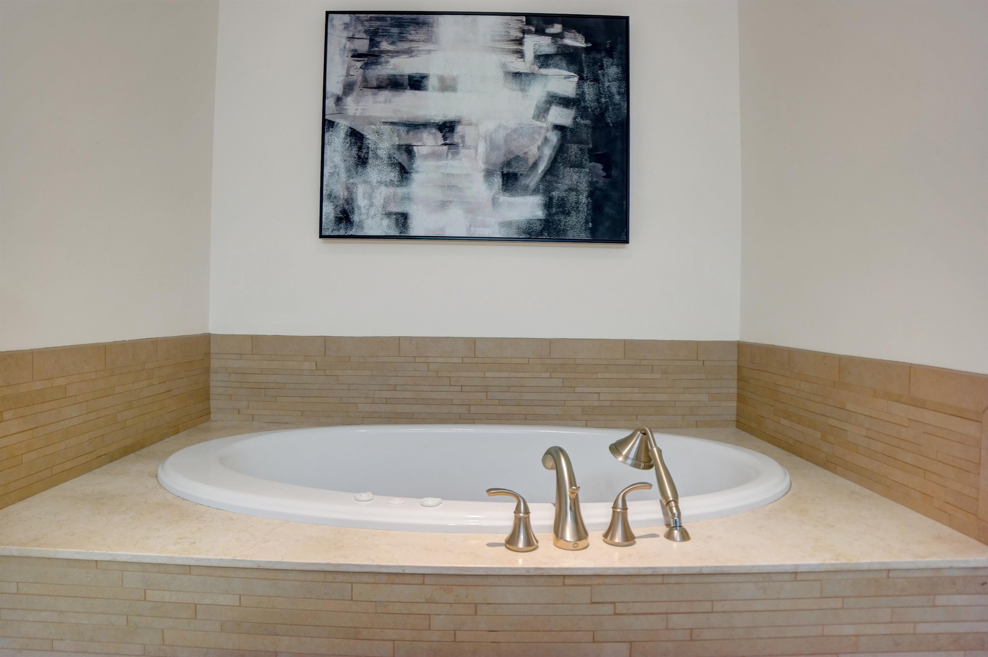 Large soaking tub with neutral tile surround, brushed metal fixtures and contemporary artwork above.