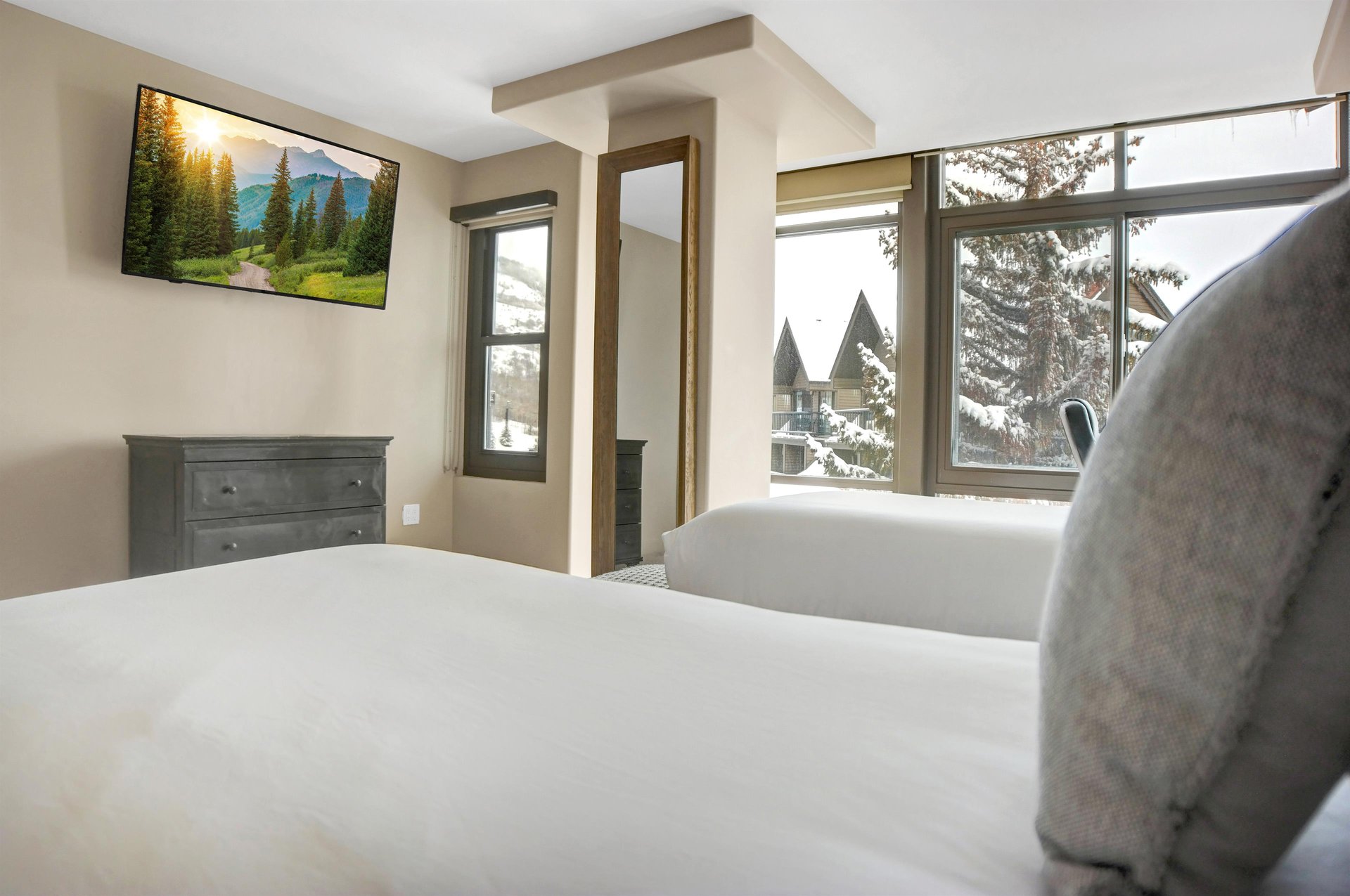 Bright guest bedroom with two twins beds, wallmounted TV and large windows overlooking the snowy mountain scenery.