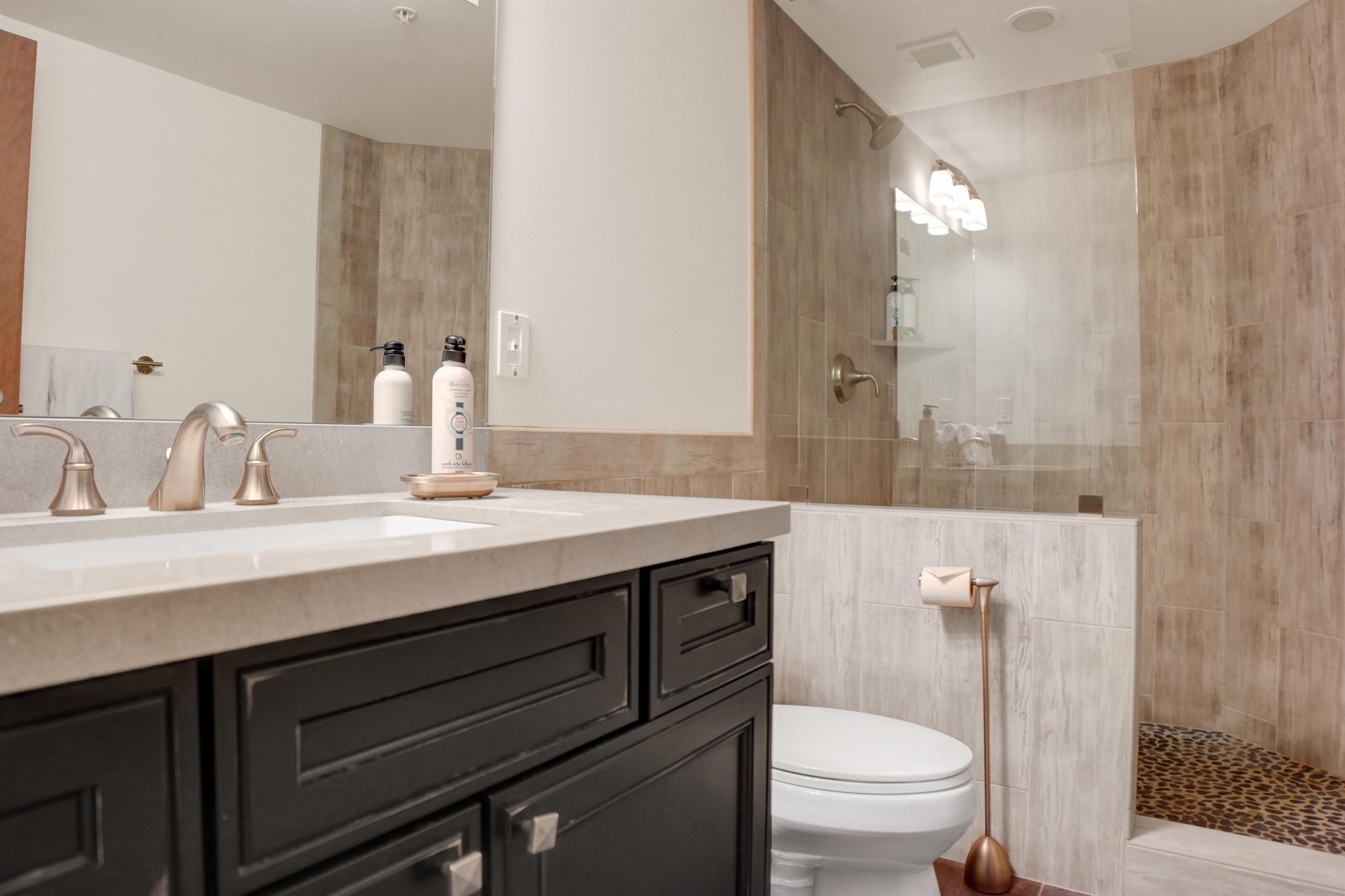 Full bathroom with dark wood vanity, stone countertop, large mirror and glassenclosed walkin shower.
