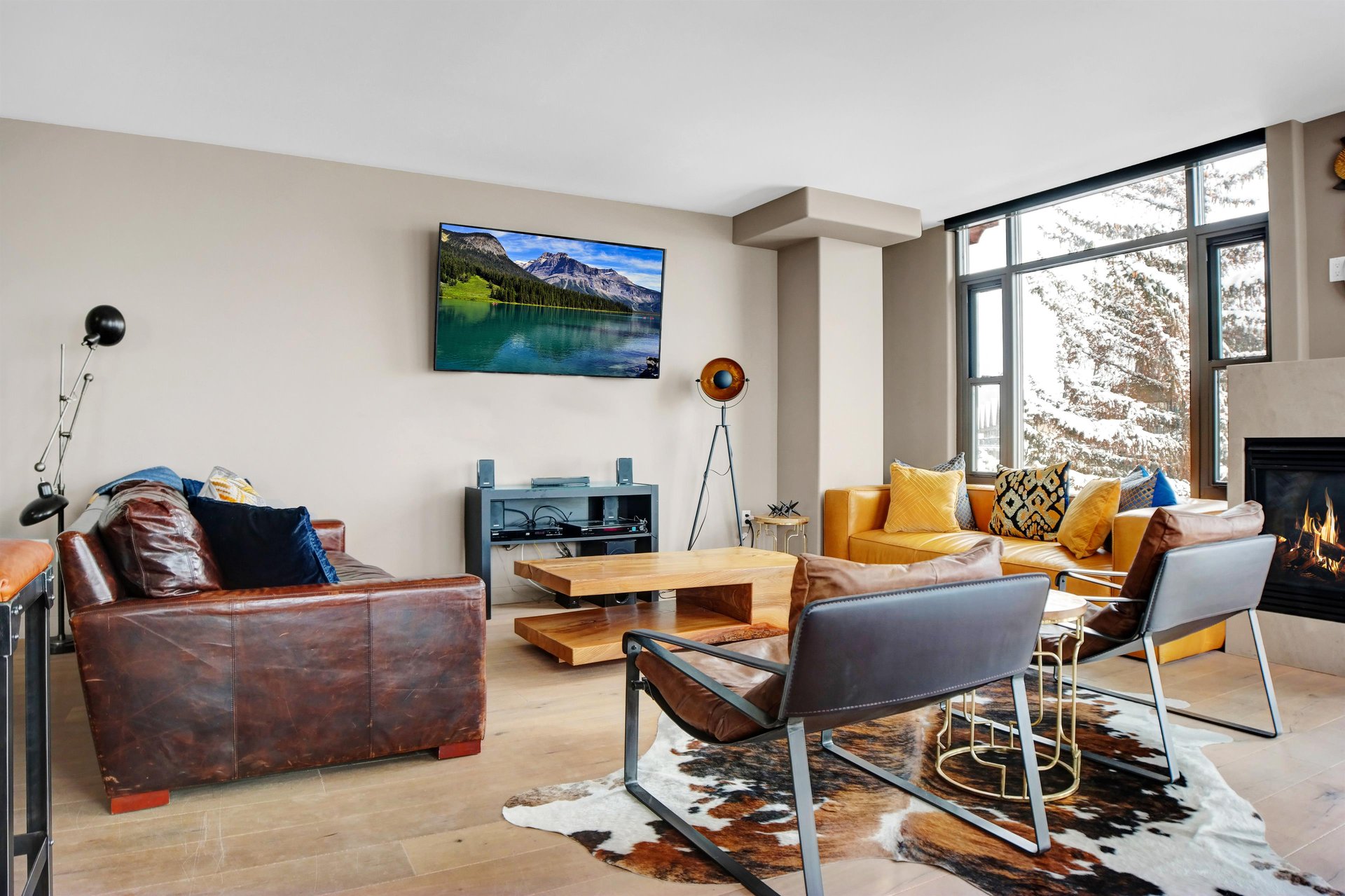 Bright living room with comfortable seating, TV and large windows overlooking the mountain surroundings.