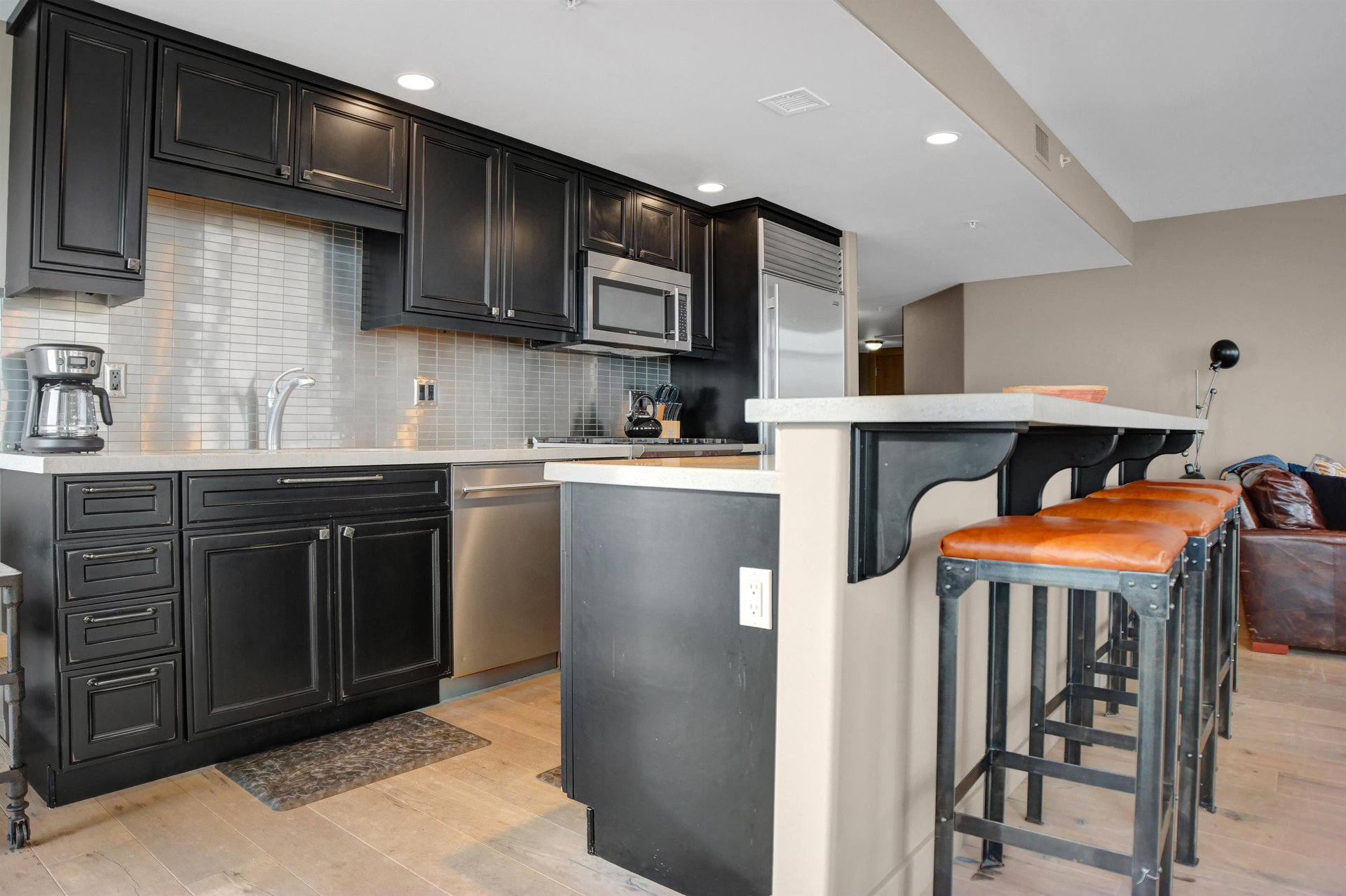 Modern kitchen with dark cabinetry, stainless steel appliances, stone counters and breakfast bar seating.