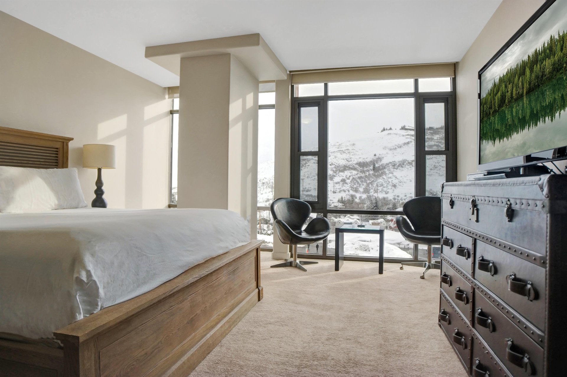Spacious king bedroom with sitting area and floortoceiling windows overlooking the snowy mountains.