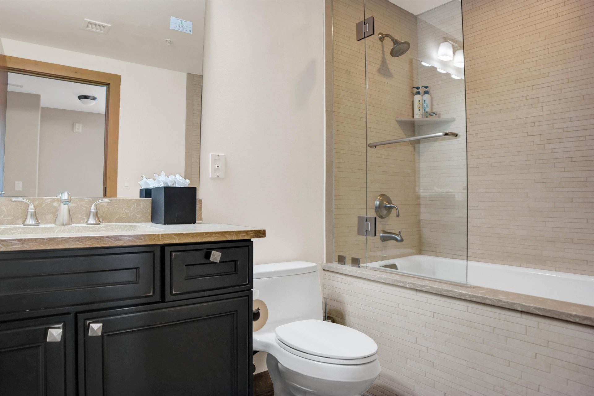 Bathroom with tub and shower combination, toilet, vanity and modern dark cabinetry.