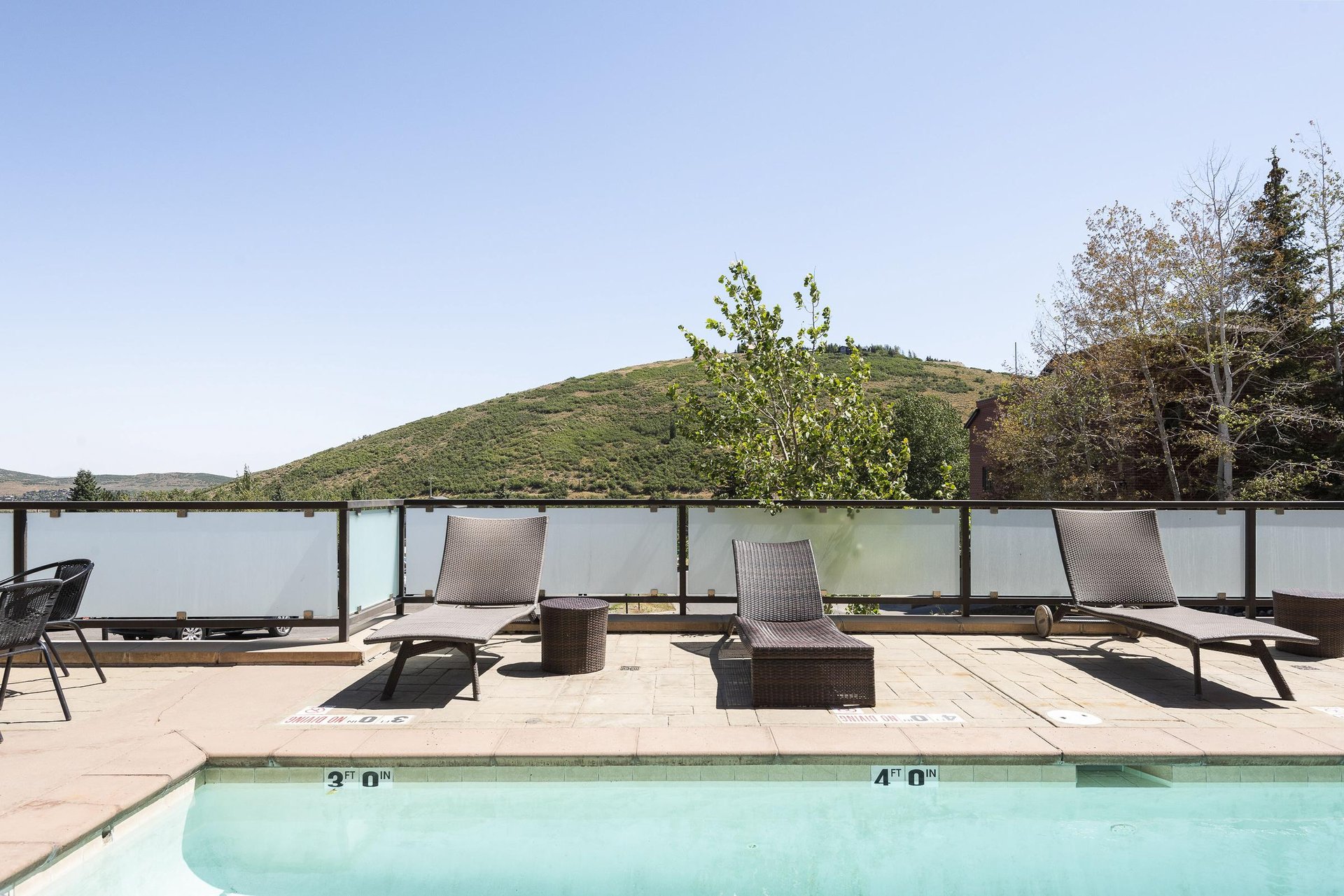 Outdoor pool deck with lounge seating and green mountain views during summer.