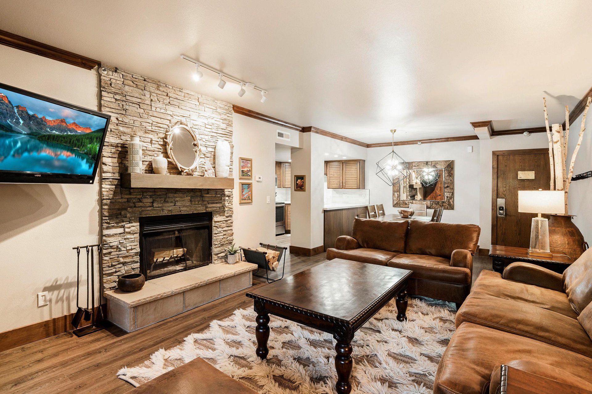 Cozy living room with stone fireplace, leather seating, wood coffee table and warm mountain decor.
