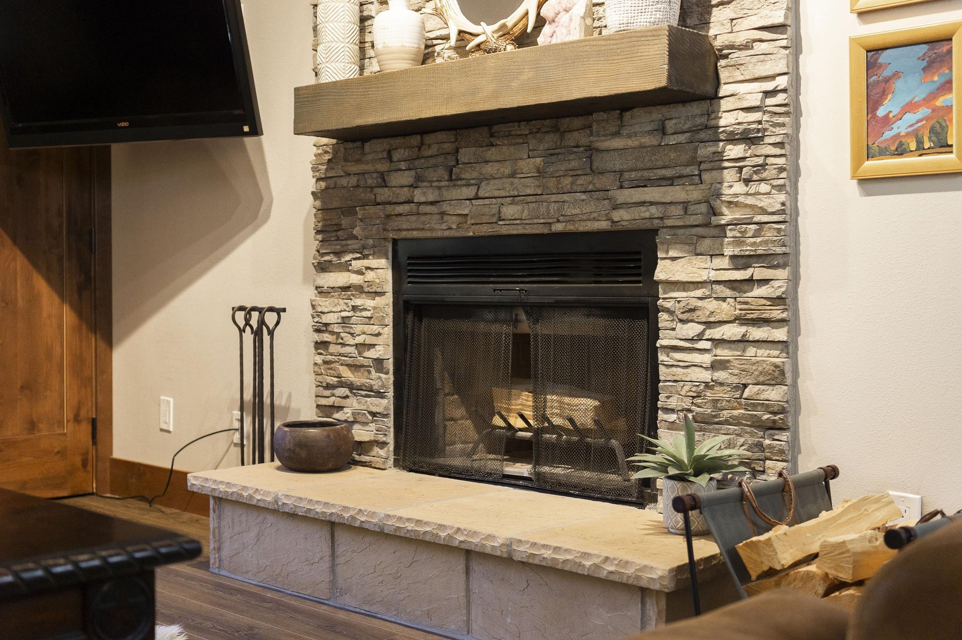 Stone woodburning fireplace with raised hearth and fireplace tools for cozy evenings.