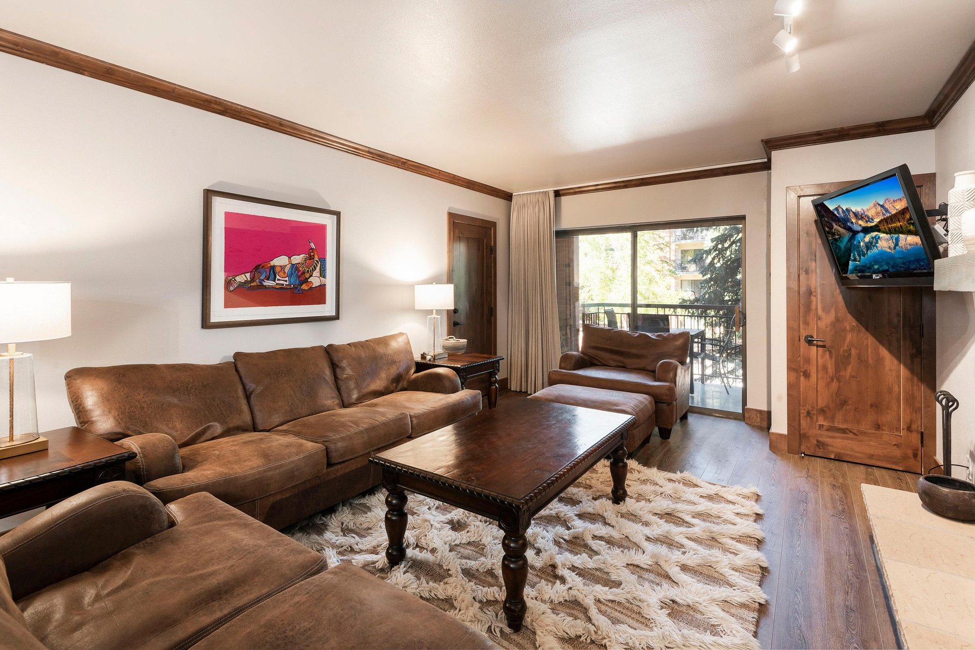 Spacious living room with leather sectional, wood coffee table, area rug and large windows.