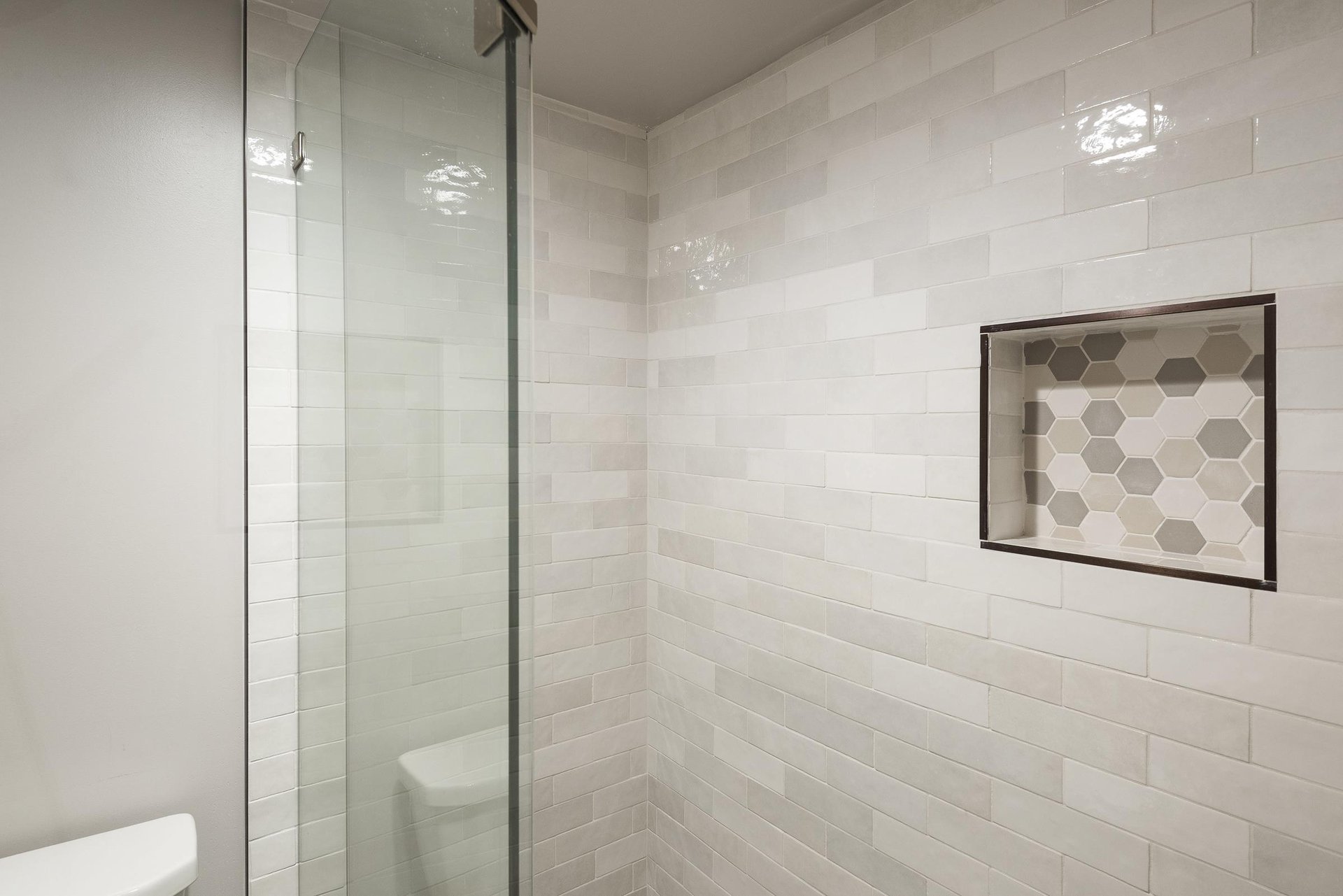 Glassenclosed walkin shower with white tile surround and builtin shower niche.