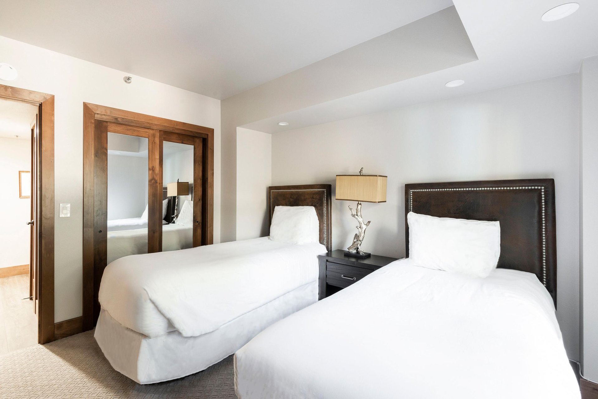 Bedroom with two beds, crisp white linens, shared nightstand and warm wood accents.