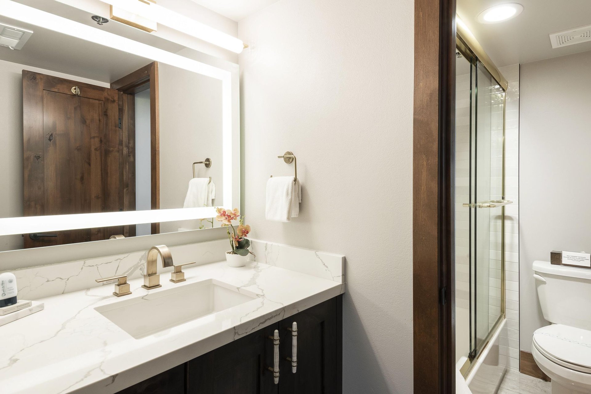 Guest bathroom with dark wood vanity, white countertop, illuminated mirror and glass shower.