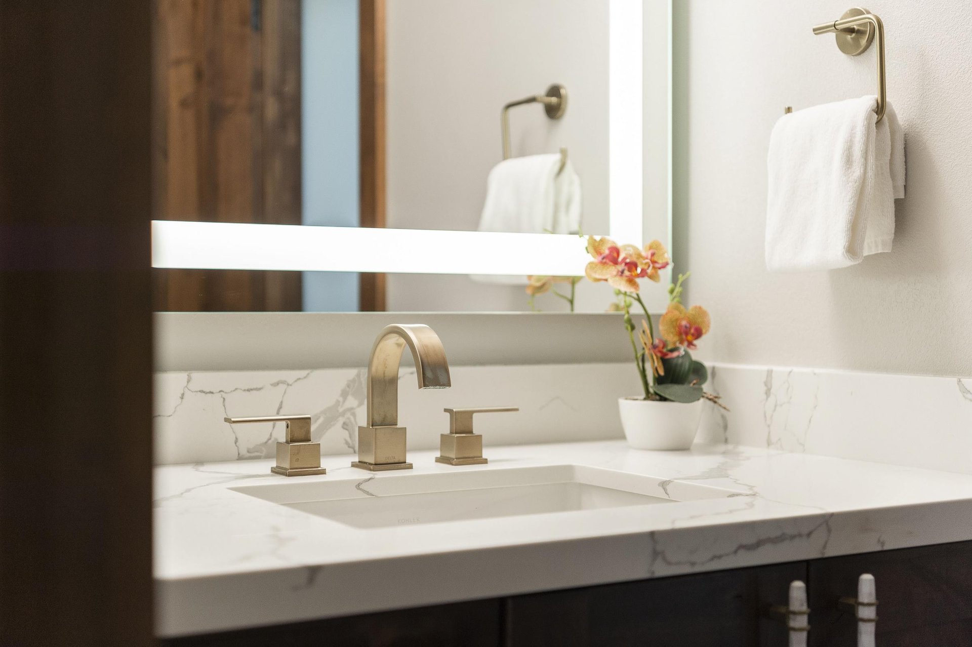 Bathroom vanity with white stone countertop, modern fixtures and illuminated mirror.