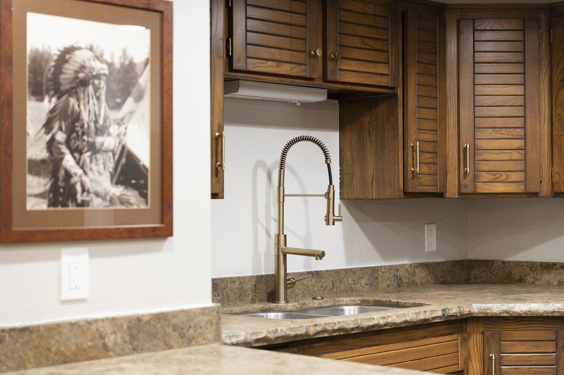 Kitchen sink with granite countertop, modern faucet, tile backsplash and wood cabinetry.