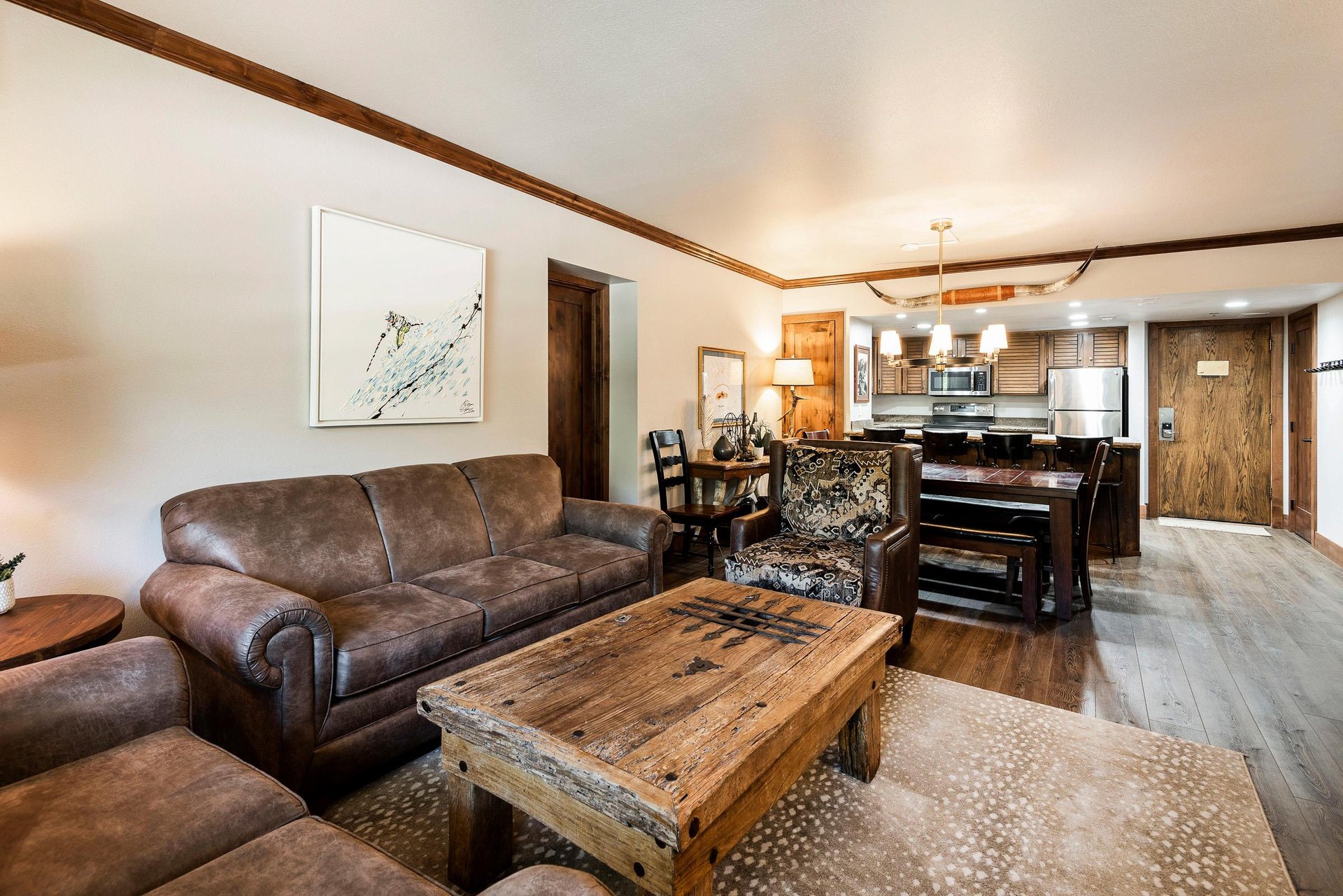 Open living and dining area with leather sofa, rustic wood coffee table and kitchen in the background.