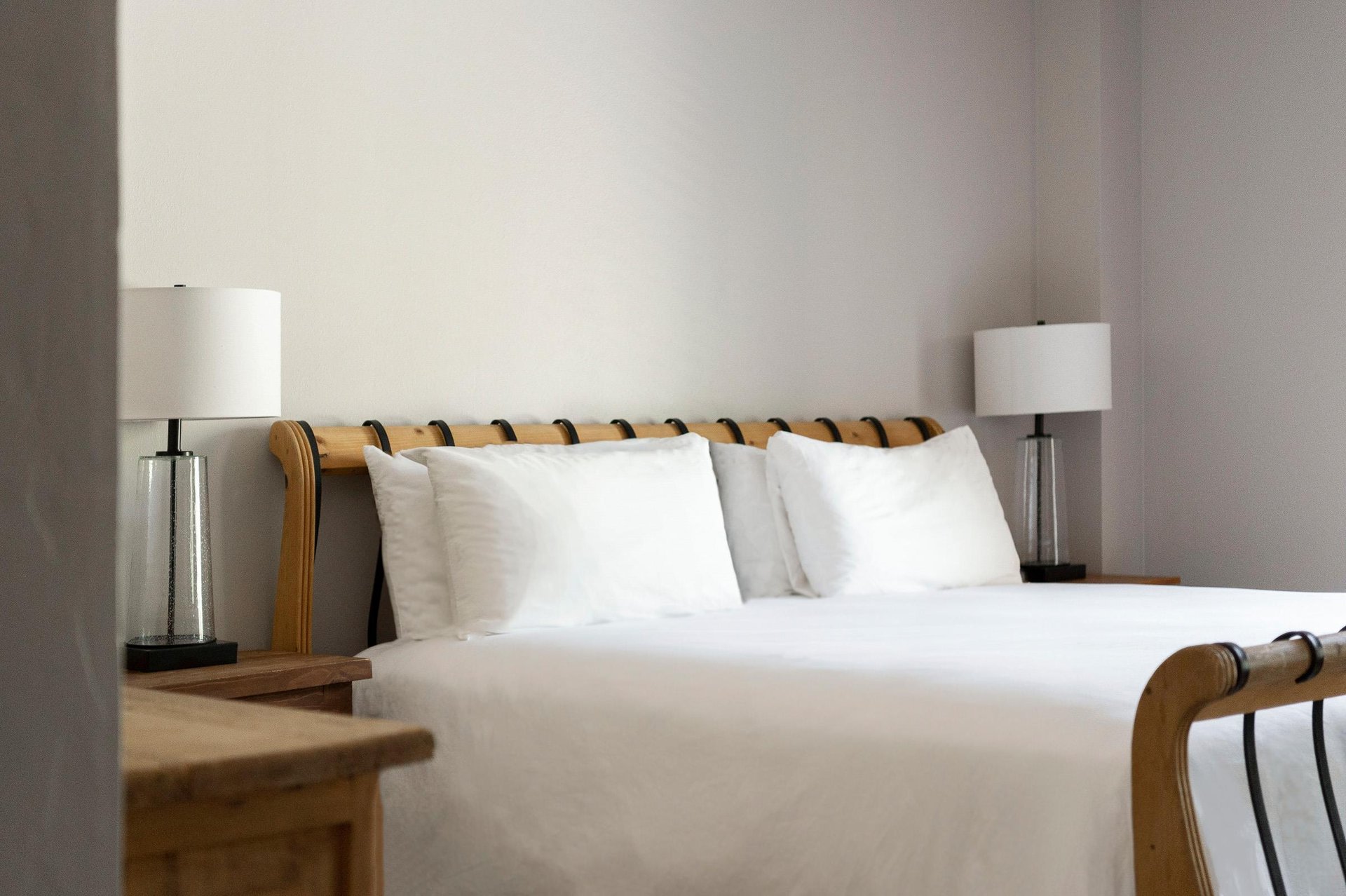 Woodframed bed with crisp white linens, bedside tables and lamps in the primary bedroom.