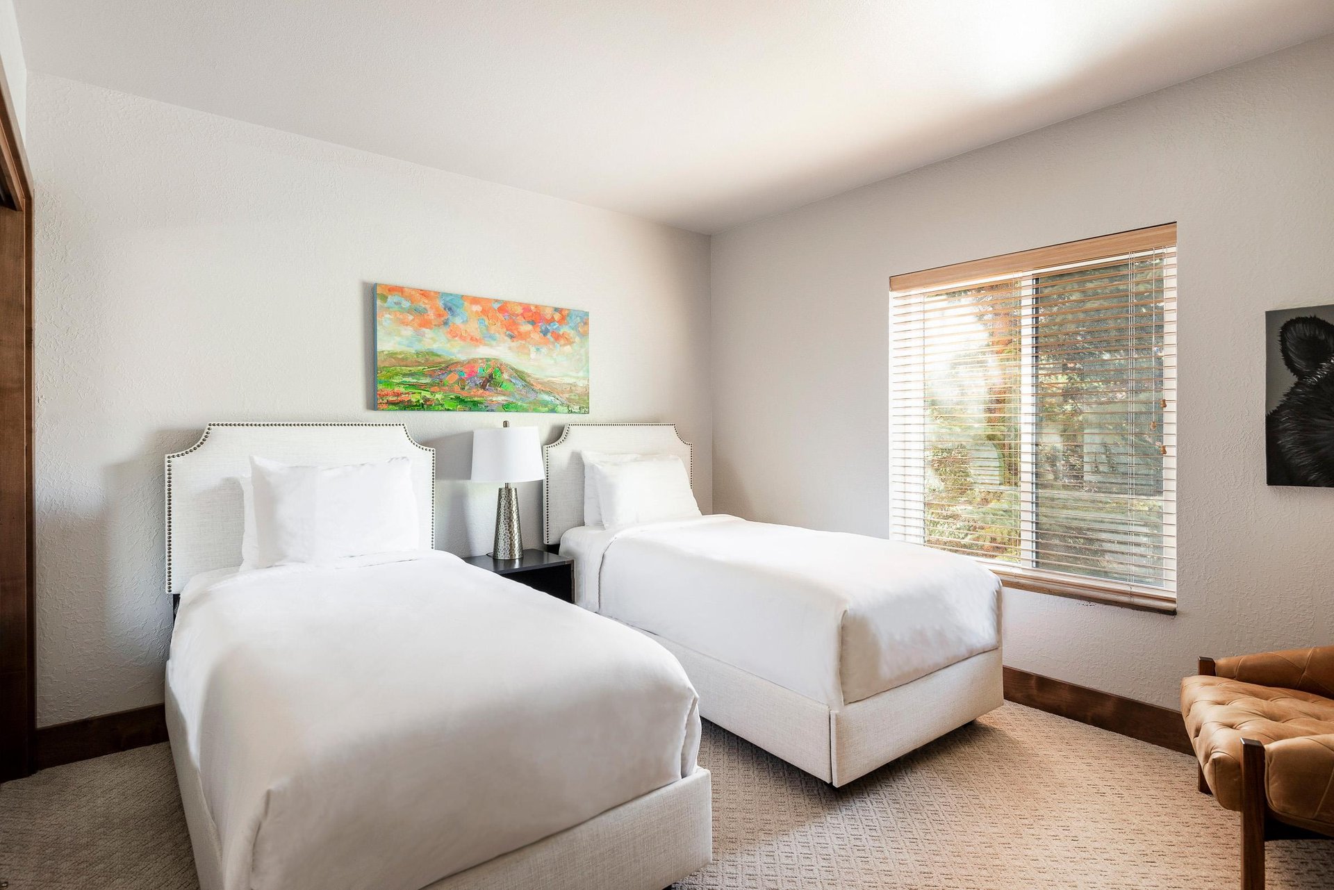 Guest bedroom with two beds, white linens, shared nightstand and large window with natural light.