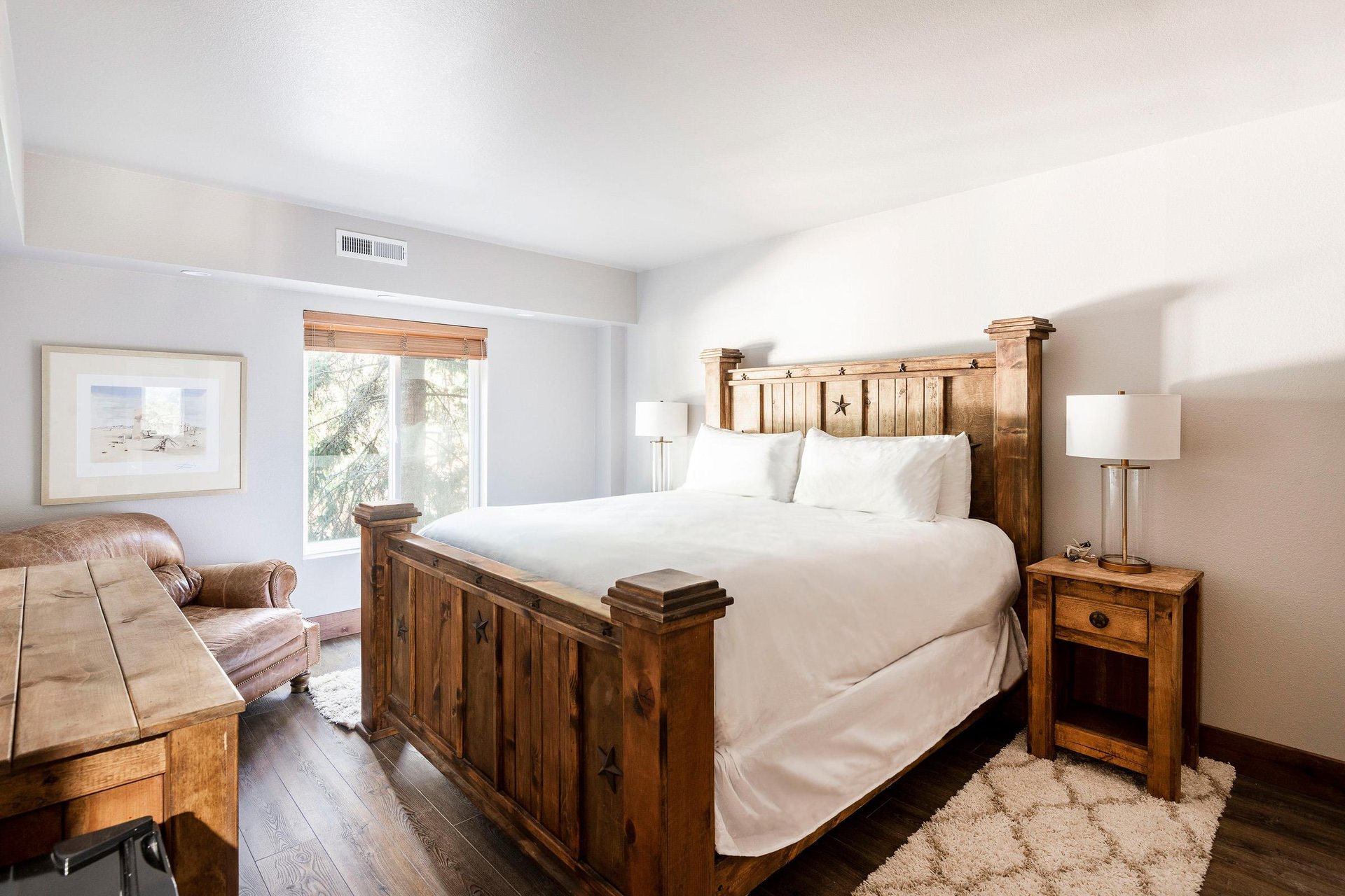 Unit 227 primary bedroom with rustic wood bed, white linens, nightstands and natural light.