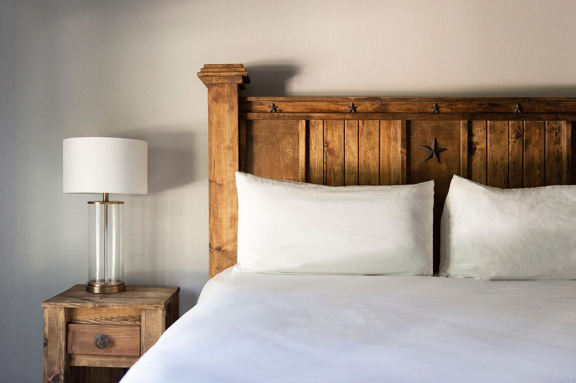 Unit 227 rustic wood bed with crisp white linens, carved headboard and bedside lamp.