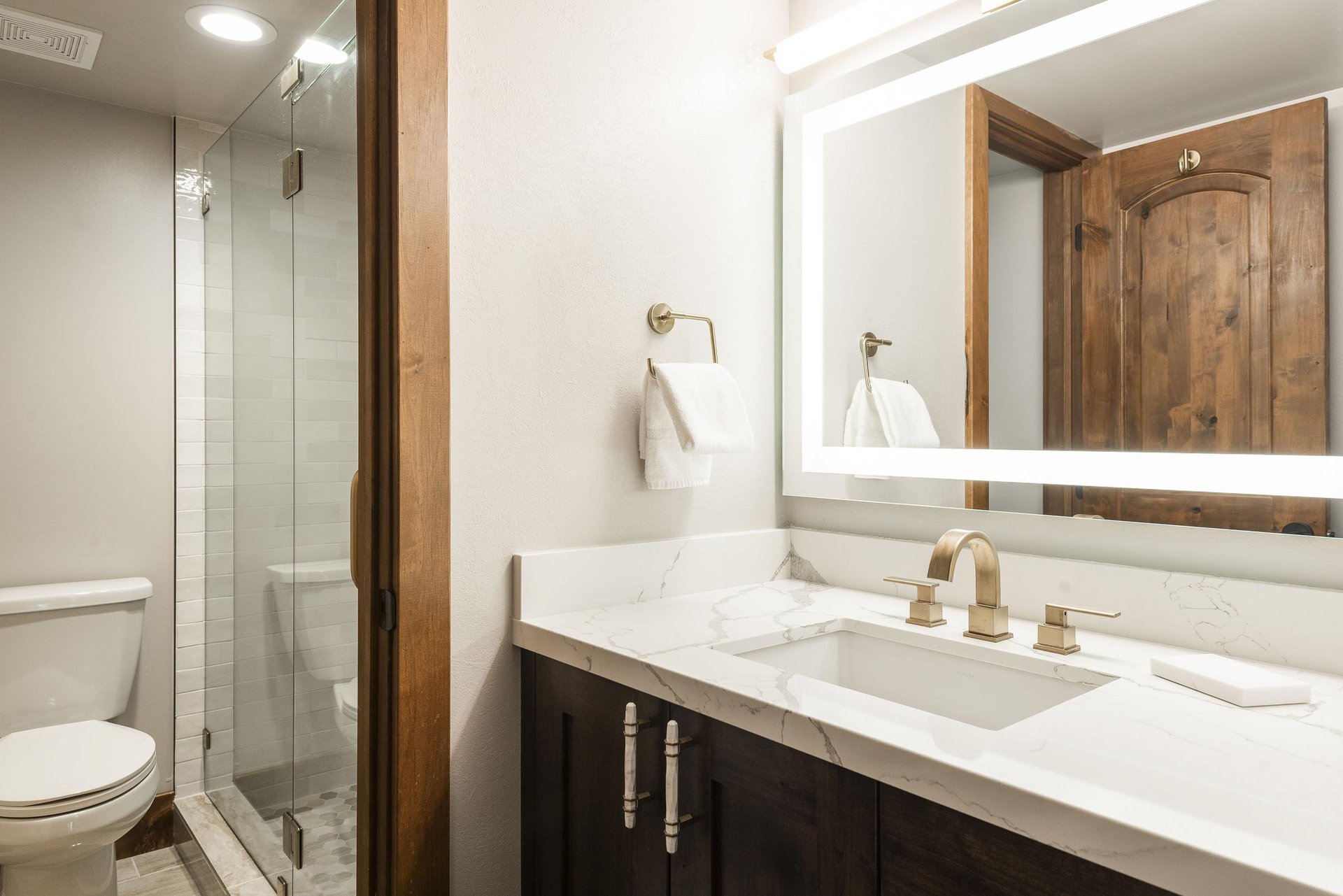 Unit 227 ensuite bathroom with dark wood vanity, white countertop, illuminated mirror and glass shower.
