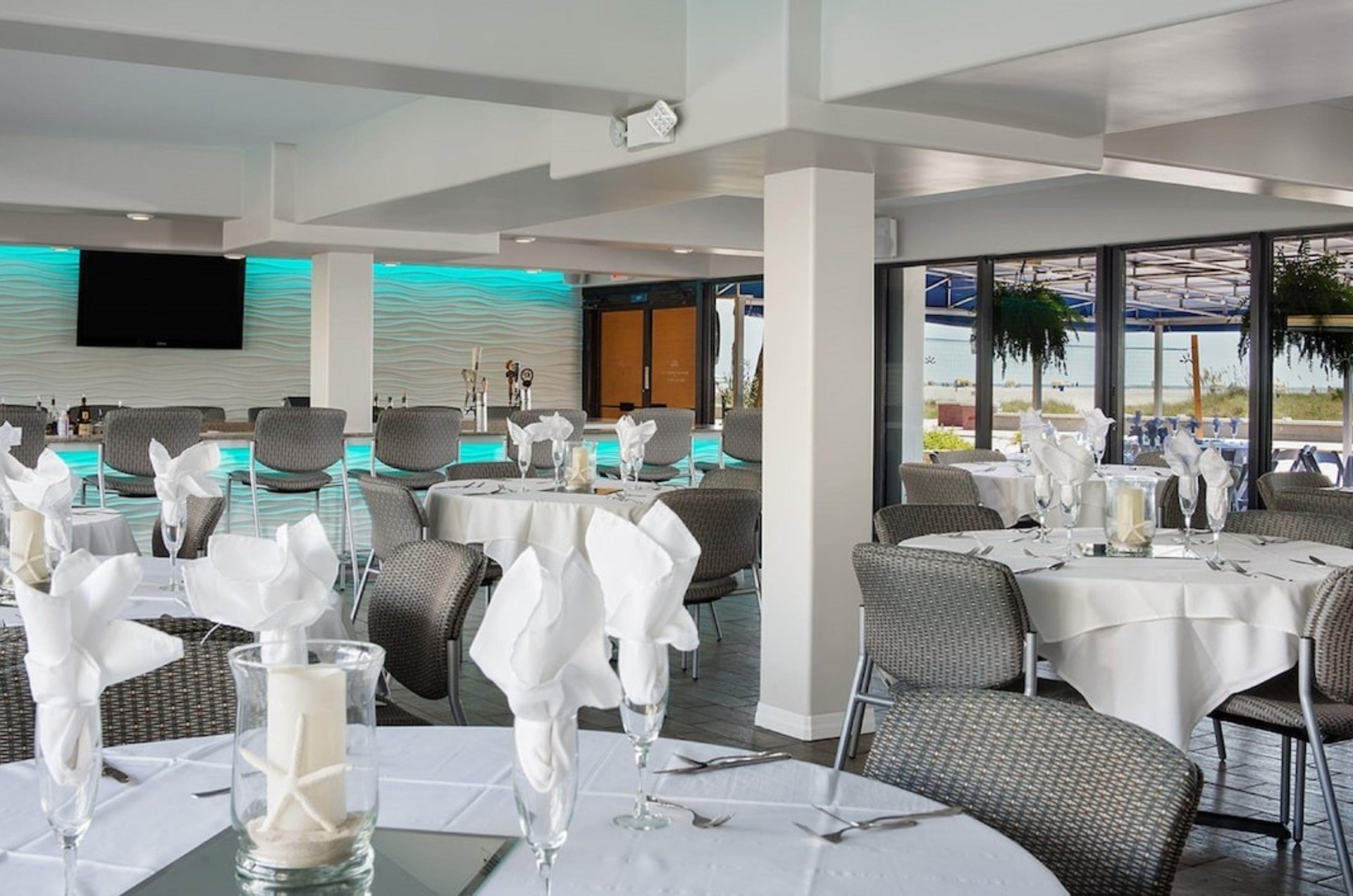 Elegant tables next to beachfacing windows and the bar in the event space at Bilmar Beach Resort