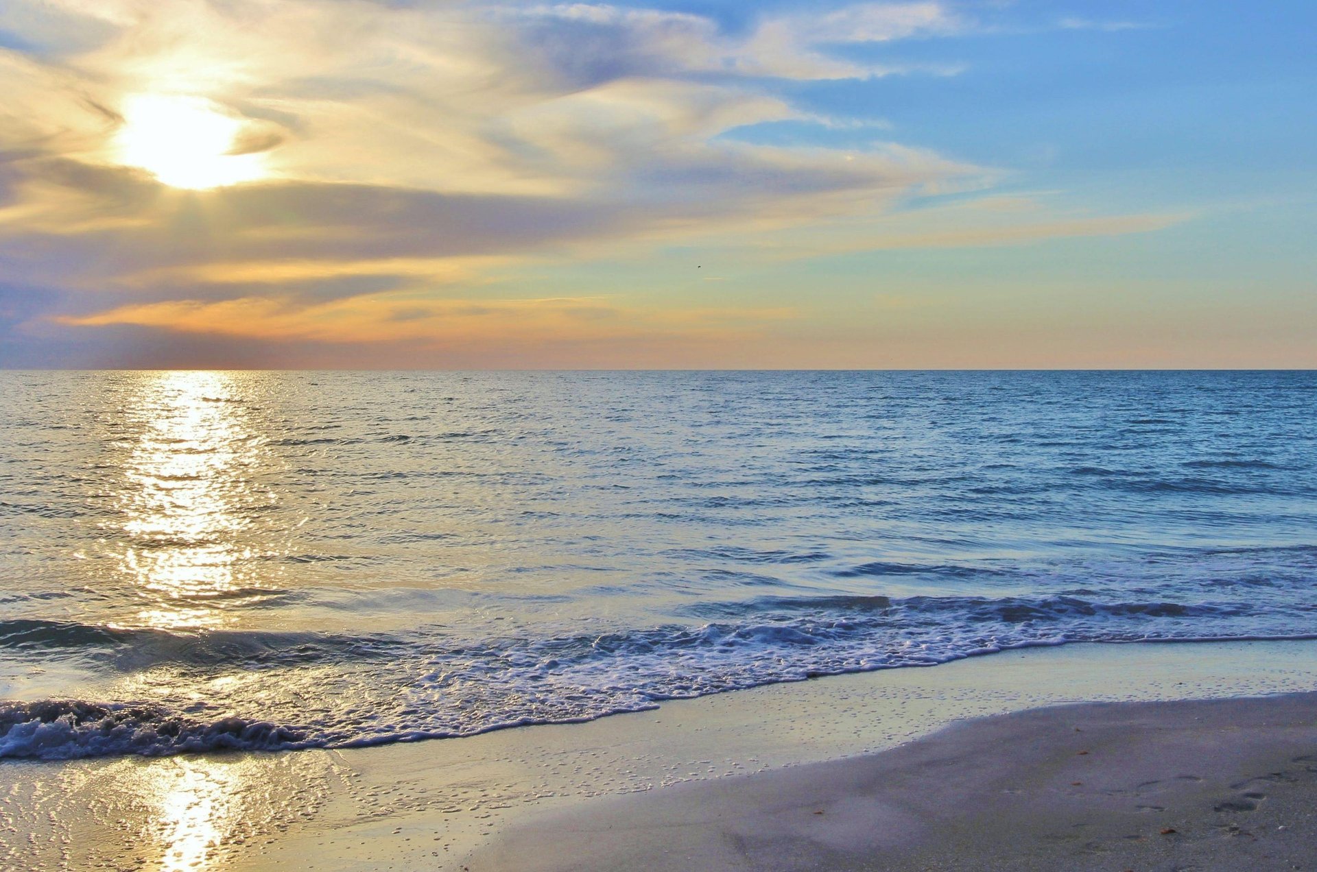 The sun setting over the Gulf as waves lap the shore.