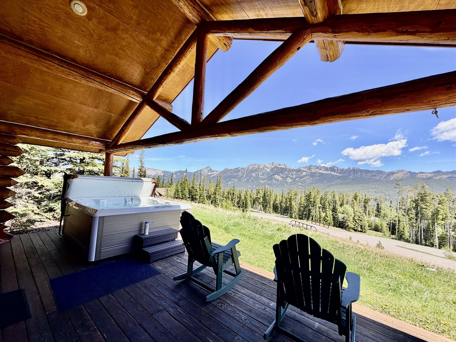 a deck with chairs and a table on it with a view of a forest and mountains in the