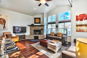 Living room with two leather couches, flagstone wood burning fireplace, and large screen TV, hardwood floors thourhout with accent rug