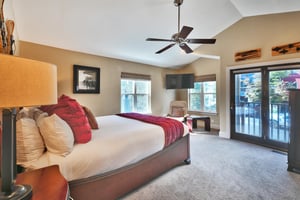 King bed in the main bedroom with white duvet and red accent linens, wood bedframe and glass patio door to private deck