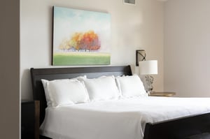 King bed in the main suite, luxurious white linens and duvet, bedside glass lamp and wall sconce lighting
