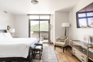 Main bedroom large flat screen wall mounted TV, accent armchair, and sliding glass doors for private deck access