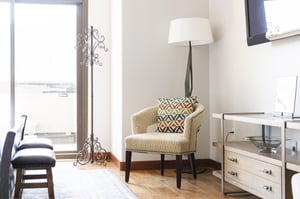 Main suite with abundant natural light, patterned cream colored armchair with modern floor lamp and iron coat rack