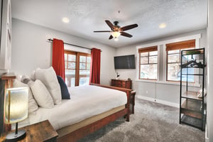 Queen guest bedroom, white linens, red drapes framing the private patio, wall mounted TV