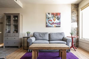 Grey sleeper sofa with modern colorful art piece in the living room and grey wood hutch with glass cabinets