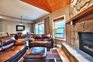 Living room, dark brown leather couches with leather footstool, large area rug and natural light with large picture window and patio doors