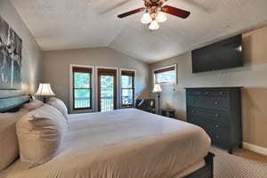 Main bedroom suite with wall mounted flat screen TV, dark wood dresser and black leather accent chair