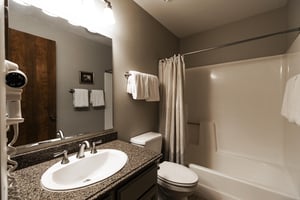 Shared guest bathroom includes dark granite countertops and a bathshower combination with a shower curtain