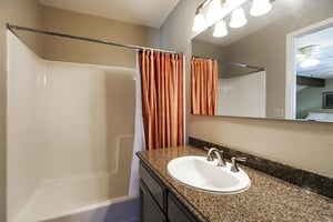 Loft bathroom has dark granite countertops and a bathshower combination with a burnt orange shower curtain