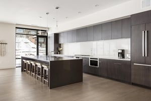 Stunning chefs kitchen with dark quartz kitchen island and barstool seating, white quartz countertops and backsplash, panel ready refrigerator and dark wood cabinetry