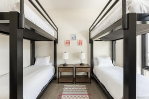 Double bunk room with wooden side tables, hardwood floors and rug runner