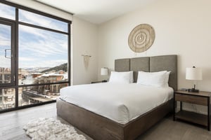 Guest bedroom with wood platform bed, suede headboard and stunning window walls with views of the resort plaza