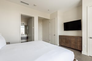 Luxurious king bed with wooden dresser, ensuite bath, two closets and wall mounted TV