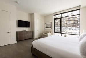 King bed with white duvet, wooden dresser, two closets, wall mounted TV and windows overlooking the pool and ski hill