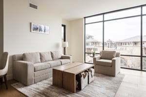 Bright open living room with private patio access, large sofa and accent chair, wooden coffee table and rectangular cowhide poufs