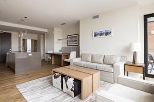 Living room opening up to the kitchen and dining area, living room has large white luxurious sofa, solid wood coffee table with cowhide poufs and large area rug
