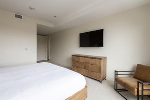 Main bedroom king bed, wall mounted TV, wooden dresser, and leather accent armchair
