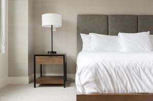 Wood and metal storage nightstand with tall bedside lamp, suede tufted headboard at the king bed