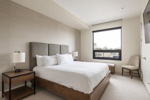Guest bedroom with king bed, picture window, wooden bedside table and accent chair