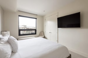 King bed in the guest bedroom with white duvet and linens, closet, wall mounted flat screen TV