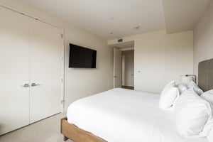 Guest bedroom with French closet doors, white duvet and linen, wall mounted flat screen TV
